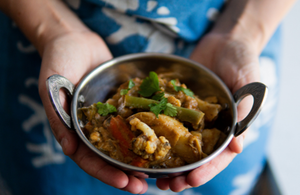 Two hands hold a bowl of vegetable curry