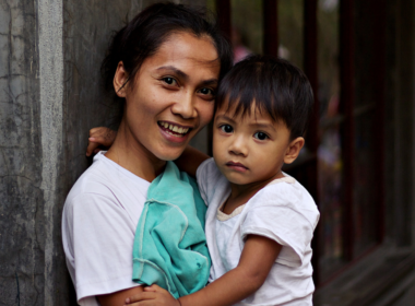 A woman smiles and holds a toddler in her arms.