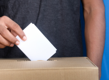 A closeup image of a man putting a vote in a ballot box.
