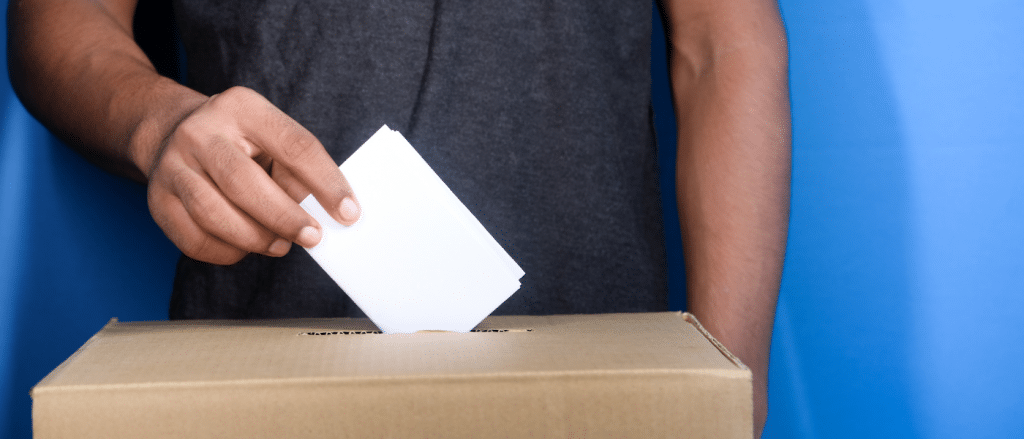 A closeup image of a man putting a vote in a ballot box.