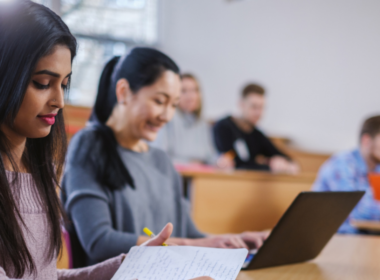 A university student sits in class, surrounded by other students.