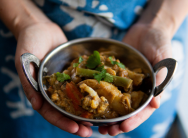 Two hands hold a bowl of vegetable curry