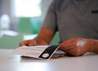 A person is sitting at a table holding a paper copy of their CV and other paperwork