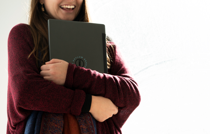 A woman in a maroon hugs a laptop close to her chest