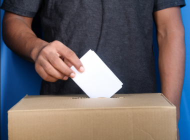 A man's hand putting a vote card in a ballot box.