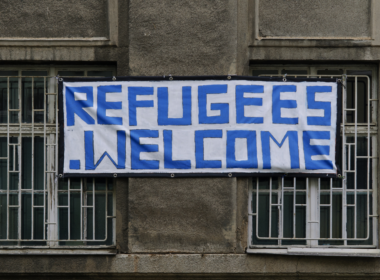 A sign on a building reads 'REFUGEES WELCOME'
