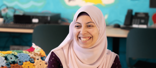 A young woman wearing a pale pink headscarf smiles