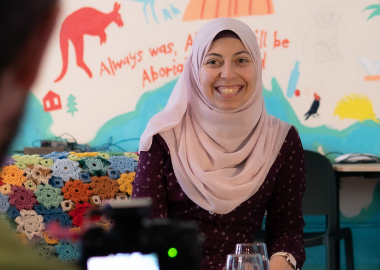 A young woman wearing a pale pink headscarf smiles into the camera.