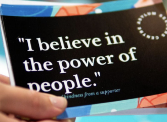 A hand holding a printed pamphlet that says "I believe in the power of people"