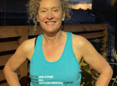 A woman wearing a blue runner's singlet stands with her hands on her hips and smiles