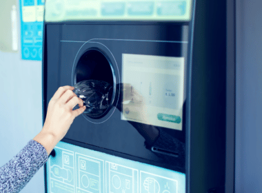 A hand pushes a plastic bottle into a recycling machine.