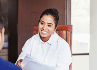 A woman with black hair and wearing a white coat smiles at a man