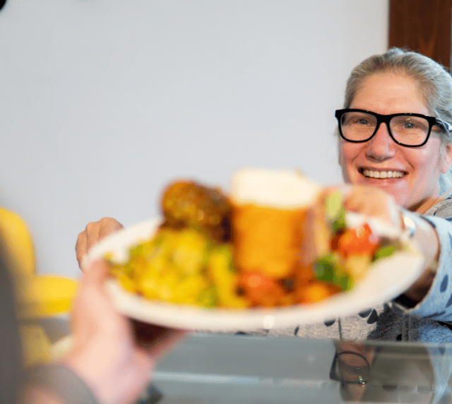 A woman serves a plate of food and smiles