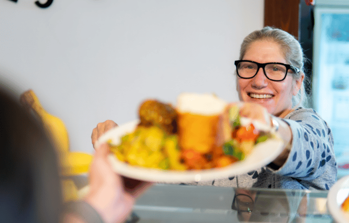A woman serves a plate of food and smiles