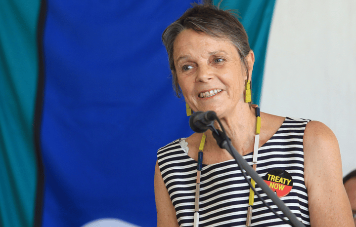 An ASC community speaker talks with a microphone, she is wearing a badge that says 'Treaty now'.