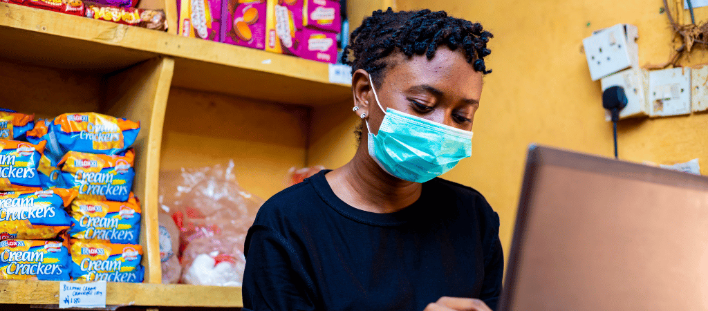 A woman works at a convenience store checkout, wearing a face mask.